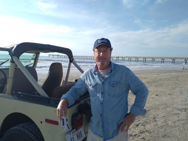 William L. Foster II — Port Aransas REALTOR® and host of Port A Insider, standing beside a vintage Jeep on the beach with Horace Caldwell Pier in the background